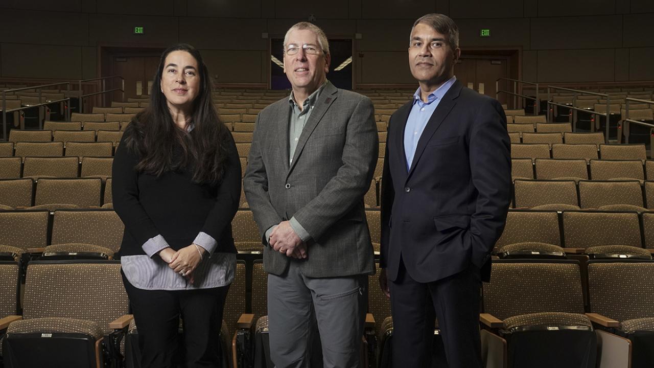 Three people are standing in an empty auditorium.