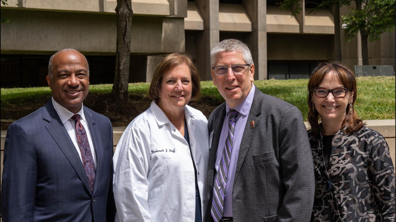 Deb Neff, in lab coat, flanked by Chancellor Gary S. May, left; and Dean Mark Winey and professor Kimberley McAllister