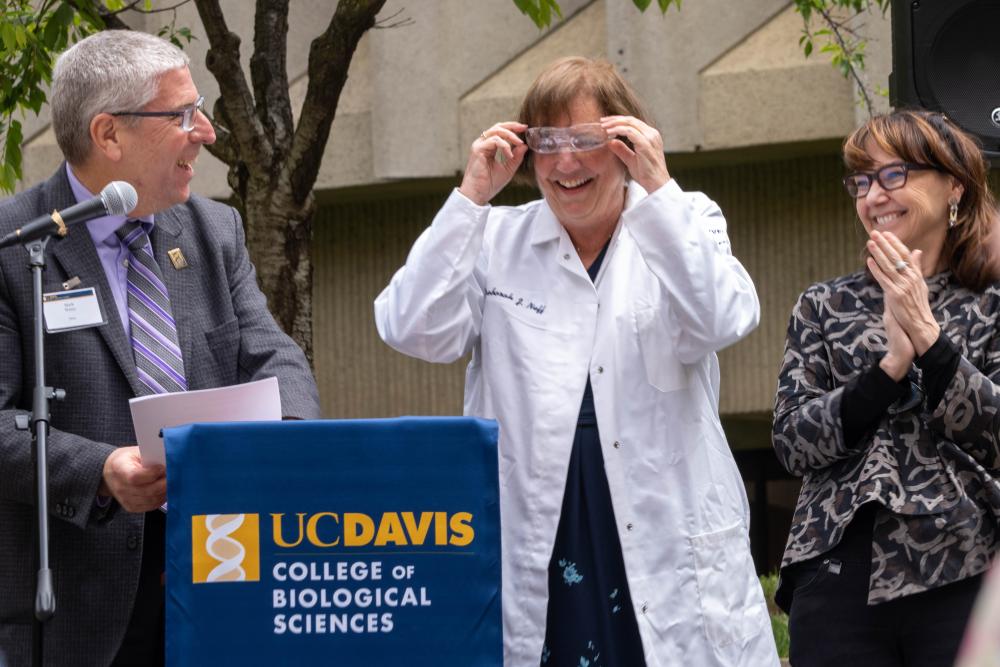 Deb Neff adjusts her safety glasses, after receiving them and a personalized lab coat from Dean Winey, left, Chancellor May and Professor McAllister, during a University Foundation Board luncheon outside Green Hall