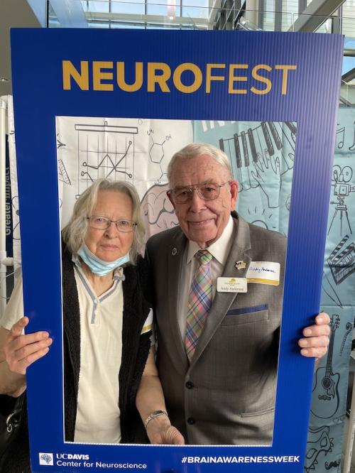 An older couple stand together holding the NeuroFest photo frame.